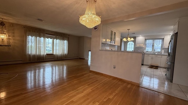 unfurnished living room with a chandelier, light wood finished floors, and baseboards