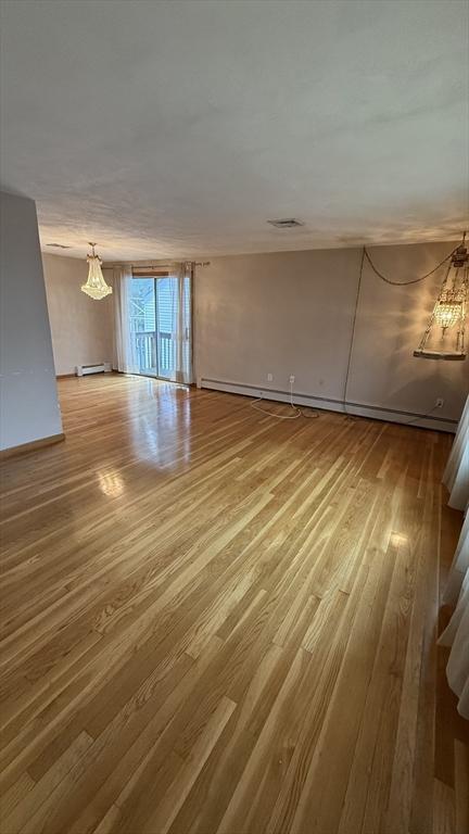 unfurnished living room featuring a chandelier, wood finished floors, baseboards, and a baseboard radiator