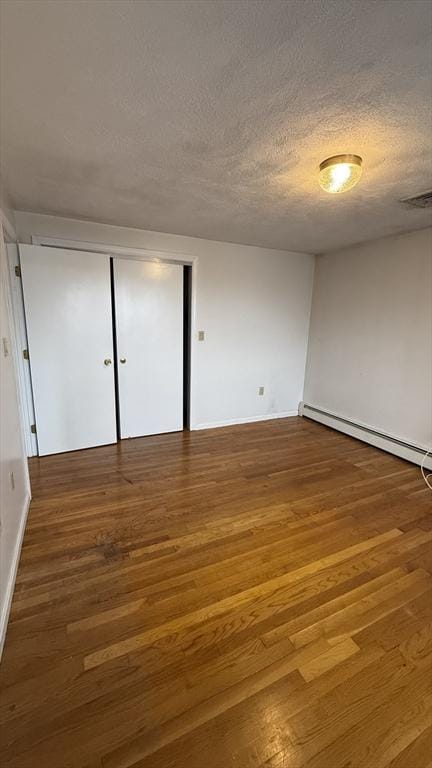 unfurnished room with wood finished floors, a textured ceiling, baseboards, and a baseboard radiator
