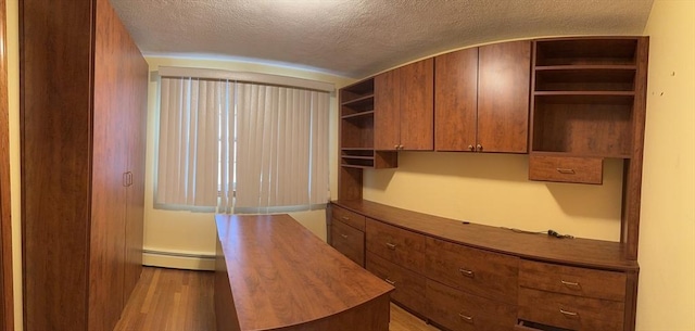 unfurnished office featuring a baseboard heating unit, a textured ceiling, and wood finished floors