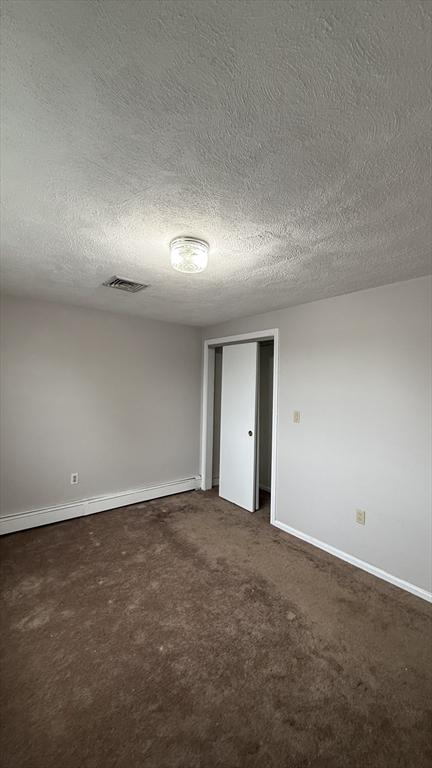 unfurnished room featuring a textured ceiling, dark colored carpet, and baseboards