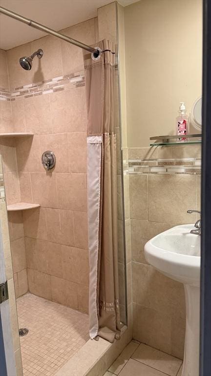 full bathroom with a shower stall, tile walls, tile patterned flooring, a sink, and wainscoting