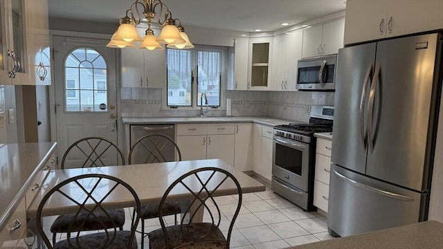 kitchen with appliances with stainless steel finishes, a sink, a chandelier, glass insert cabinets, and white cabinetry