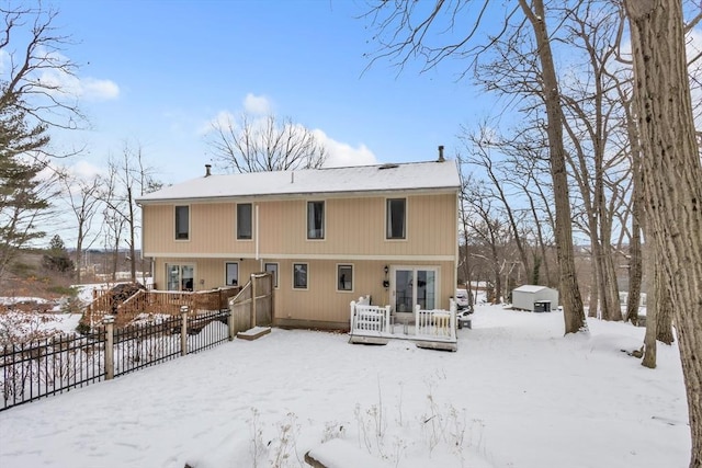 snow covered back of property with a deck, an outbuilding, a storage unit, and fence