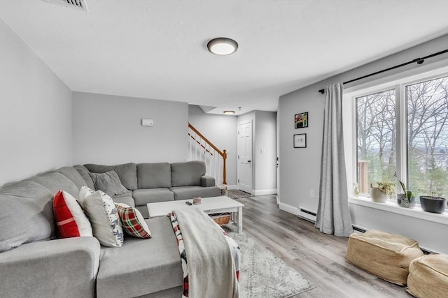 living area featuring stairway, baseboard heating, baseboards, and wood finished floors