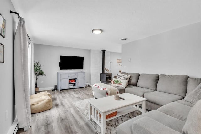 living room featuring visible vents, baseboards, light wood-style flooring, a wood stove, and a baseboard radiator