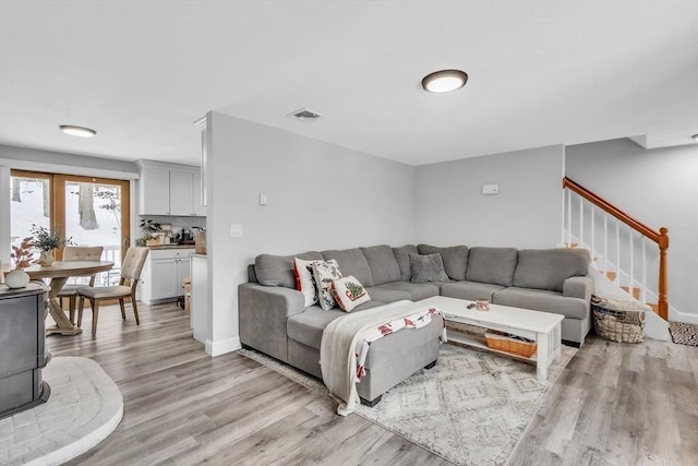 living room with visible vents, baseboards, stairs, and light wood-style floors