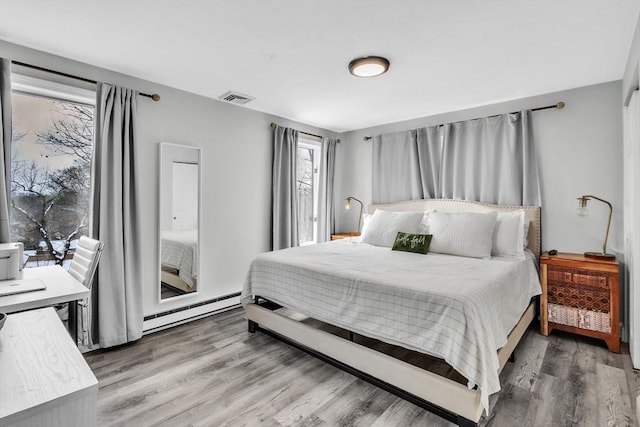 bedroom with a baseboard radiator, visible vents, and wood finished floors