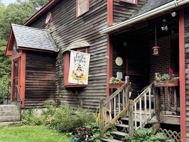 view of exterior entry with a shingled roof and brick siding