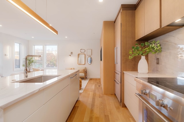 kitchen featuring light hardwood / wood-style floors, sink, light stone countertops, backsplash, and stainless steel stove