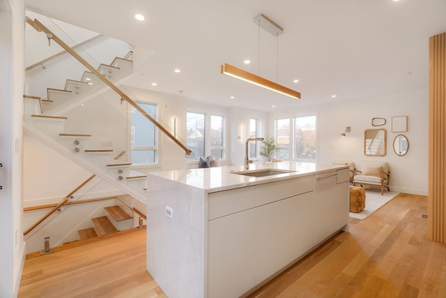 kitchen featuring light hardwood / wood-style floors, a center island with sink, sink, white cabinetry, and decorative light fixtures