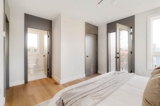 bedroom with access to outside, ensuite bath, multiple windows, and light hardwood / wood-style flooring