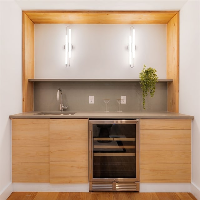 bar featuring light brown cabinets, light hardwood / wood-style floors, sink, and beverage cooler