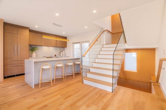 kitchen with light hardwood / wood-style floors, a breakfast bar, an island with sink, pendant lighting, and decorative backsplash