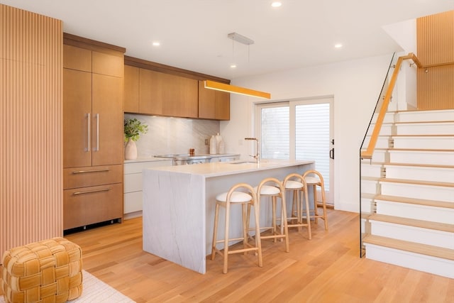 kitchen featuring sink, decorative light fixtures, an island with sink, and light hardwood / wood-style floors