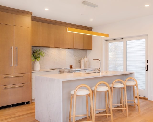 kitchen with light wood-type flooring, a breakfast bar, sink, and a kitchen island with sink