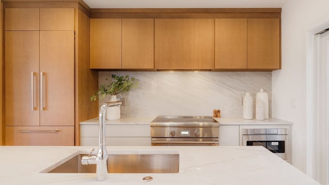 kitchen featuring appliances with stainless steel finishes, sink, backsplash, and light stone countertops