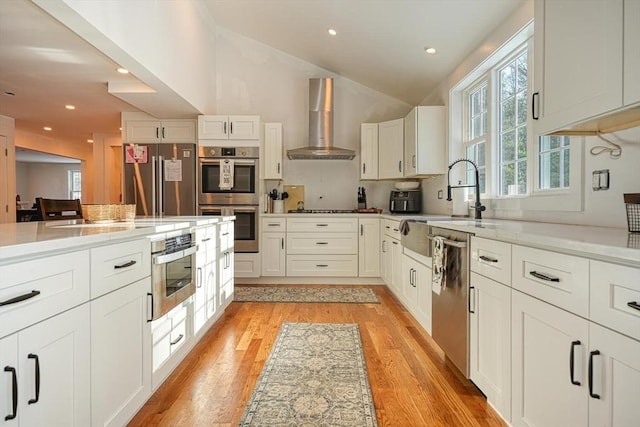 kitchen featuring appliances with stainless steel finishes, light hardwood / wood-style floors, white cabinetry, and wall chimney range hood