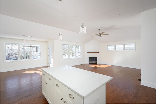 kitchen with pendant lighting, ceiling fan, white cabinets, dark wood-type flooring, and a large fireplace