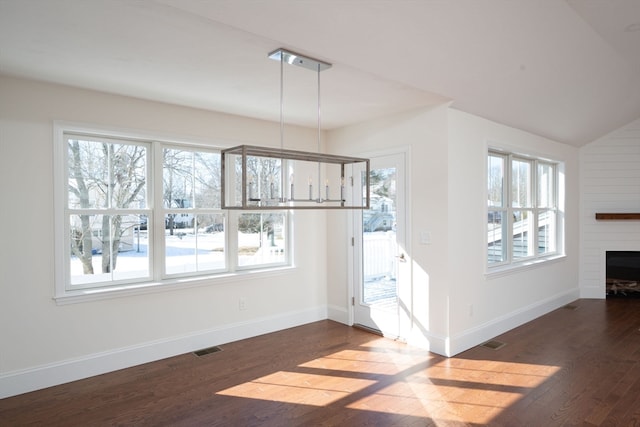 unfurnished dining area featuring a fireplace, an inviting chandelier, dark hardwood / wood-style floors, and vaulted ceiling