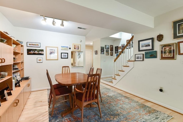 dining room featuring visible vents, rail lighting, baseboards, stairs, and light wood-style flooring