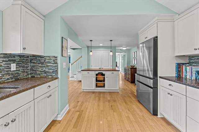 kitchen featuring freestanding refrigerator, white cabinetry, light wood-type flooring, decorative backsplash, and lofted ceiling