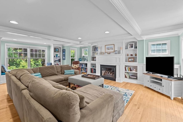 living room with ornamental molding, light wood finished floors, a glass covered fireplace, recessed lighting, and built in features
