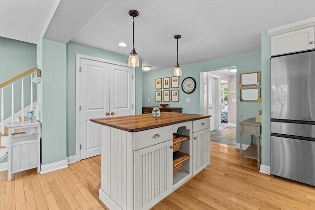 kitchen with butcher block countertops, stainless steel fridge, white cabinets, light wood finished floors, and hanging light fixtures