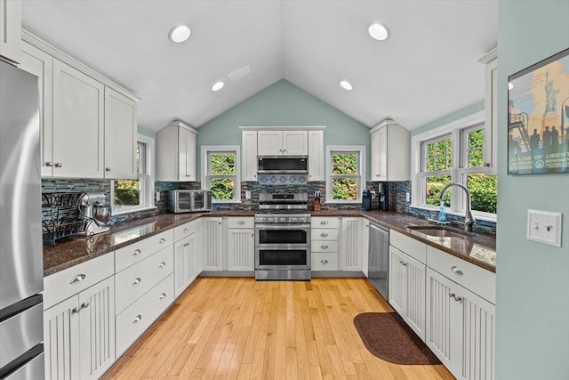 kitchen featuring stainless steel appliances, a sink, white cabinetry, vaulted ceiling, and tasteful backsplash