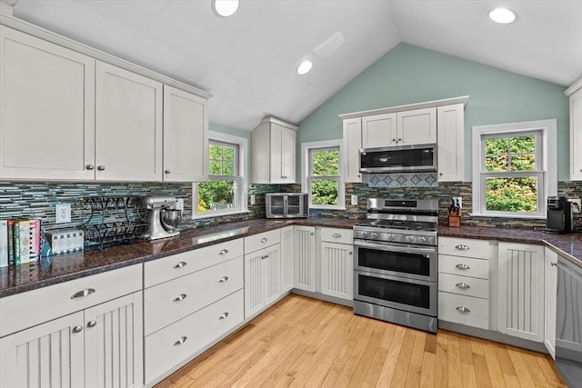kitchen with stainless steel appliances, white cabinetry, lofted ceiling, backsplash, and light wood-type flooring
