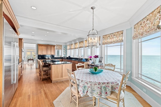 dining room featuring an inviting chandelier, a water view, a wealth of natural light, and light hardwood / wood-style flooring