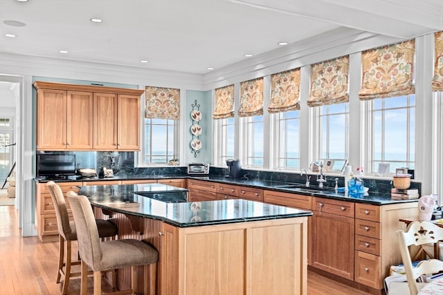 kitchen featuring a center island, backsplash, dark stone counters, sink, and light wood-type flooring