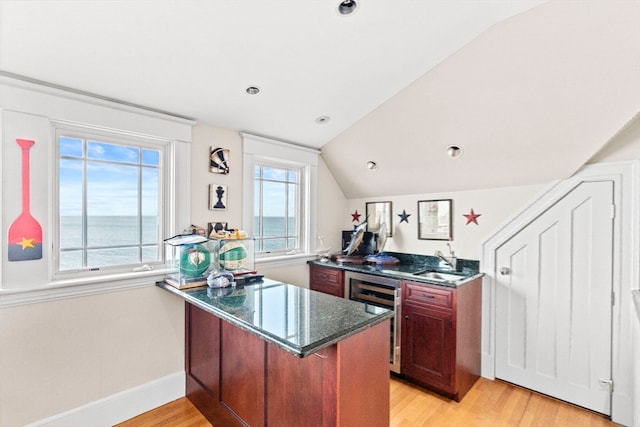 kitchen featuring beverage cooler, kitchen peninsula, light hardwood / wood-style floors, lofted ceiling, and a water view