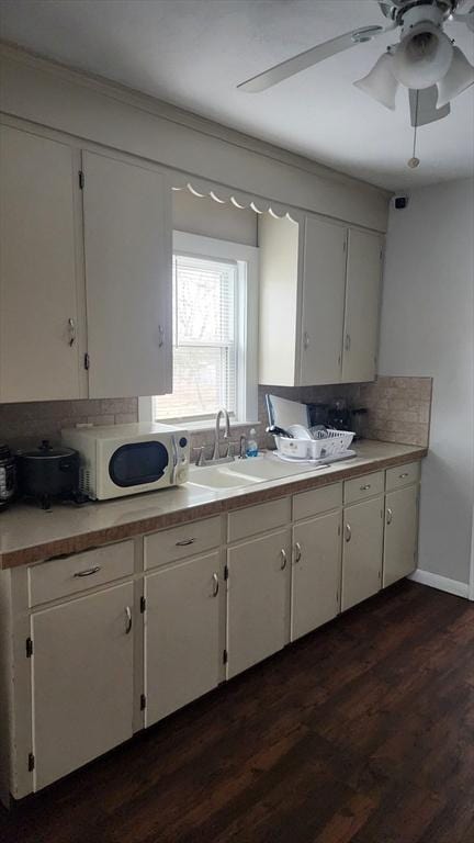 kitchen with white cabinets, white microwave, light countertops, backsplash, and dark wood-style flooring