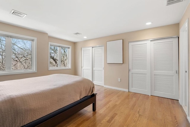 bedroom with visible vents, baseboards, light wood-style floors, and multiple closets