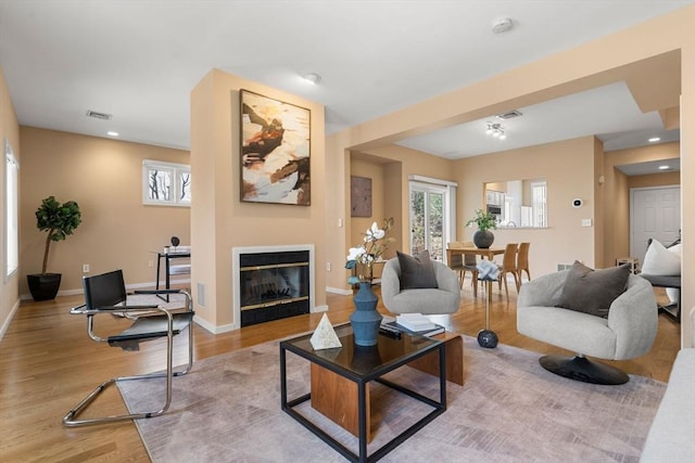 living room featuring a glass covered fireplace, light wood-style flooring, baseboards, and visible vents