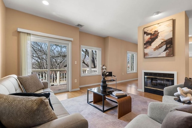 living room with visible vents, baseboards, recessed lighting, light wood-style floors, and a glass covered fireplace