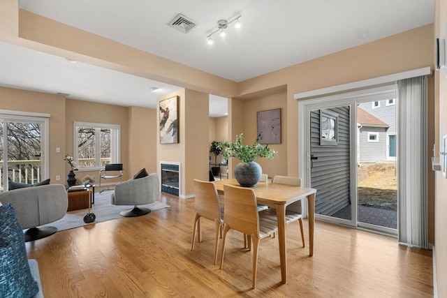 dining room with a glass covered fireplace, light wood-style flooring, and visible vents