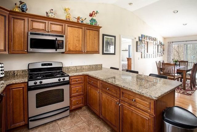 284 Hortonville Rd, Swansea, MA 02777 - kitchen featuring appliances with stainless steel finishes, vaulted ceiling, a peninsula, brown cabinetry, and light stone counters