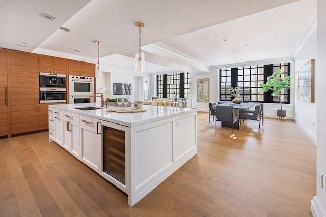 kitchen with white cabinetry, stainless steel double oven, pendant lighting, an island with sink, and beverage cooler