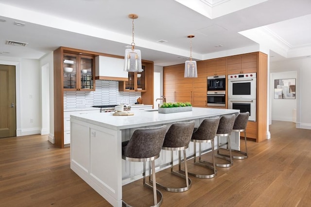 kitchen with pendant lighting, an island with sink, double oven, and tasteful backsplash