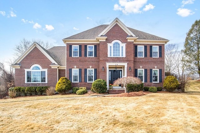 view of front of home with a front yard, brick siding, and a shingled roof