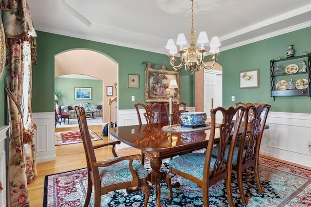 dining space with arched walkways, wainscoting, light wood finished floors, and an inviting chandelier