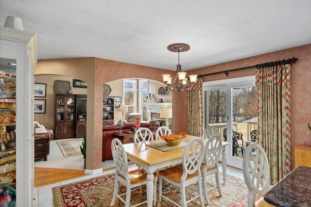 dining room with an inviting chandelier, light tile patterned floors, a fireplace, and arched walkways