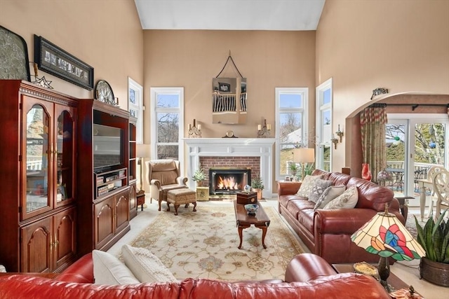 carpeted living area with plenty of natural light, a brick fireplace, and a high ceiling