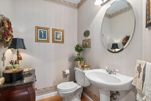 half bath featuring wood finished floors, toilet, baseboards, and a sink