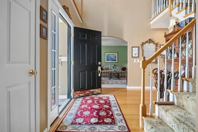 entrance foyer with light wood-type flooring, stairway, arched walkways, baseboards, and a towering ceiling