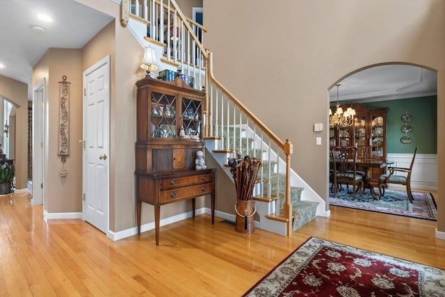 stairs featuring a notable chandelier, wood finished floors, arched walkways, and baseboards