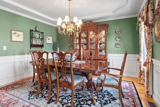 dining room featuring light wood-style floors, a raised ceiling, a notable chandelier, and a wainscoted wall