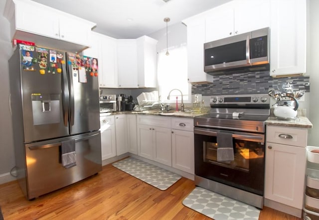 kitchen featuring white cabinetry, hanging light fixtures, backsplash, stainless steel appliances, and light hardwood / wood-style floors